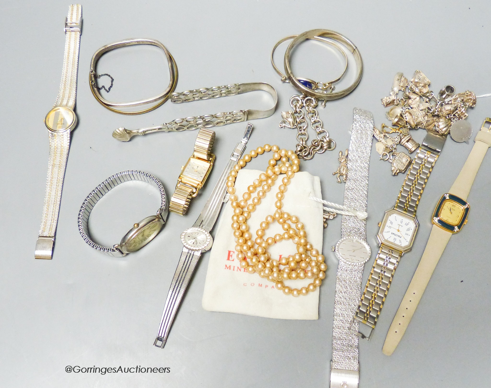 A white metal charm bracelet, five additional charms, a silver chain bracelet, four various bangles, a pair of silver sugar tongs (a.f.) and seven ladys' fashion wristwatches